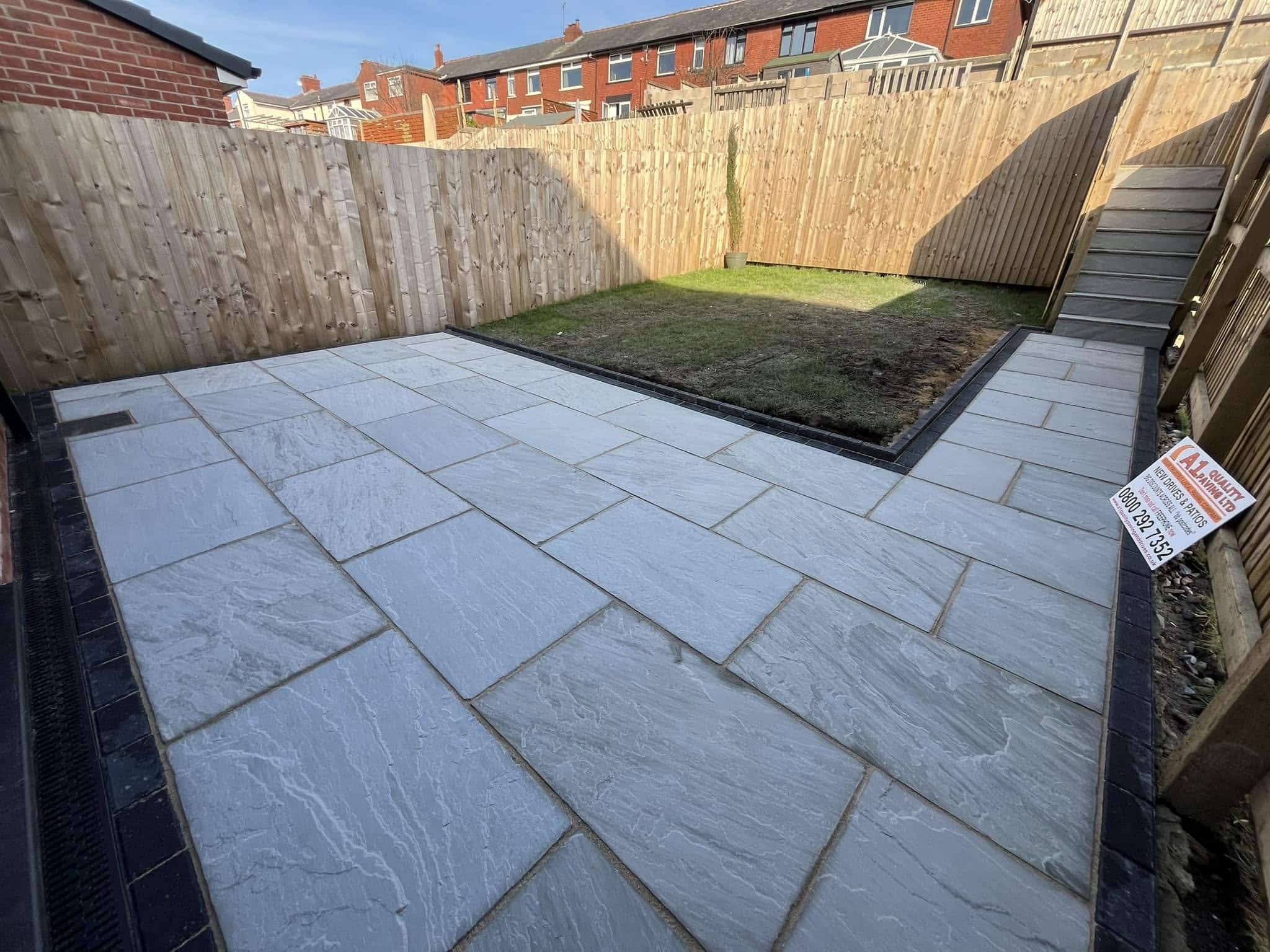 Grey riven sandstone patio with new lawn and fencing