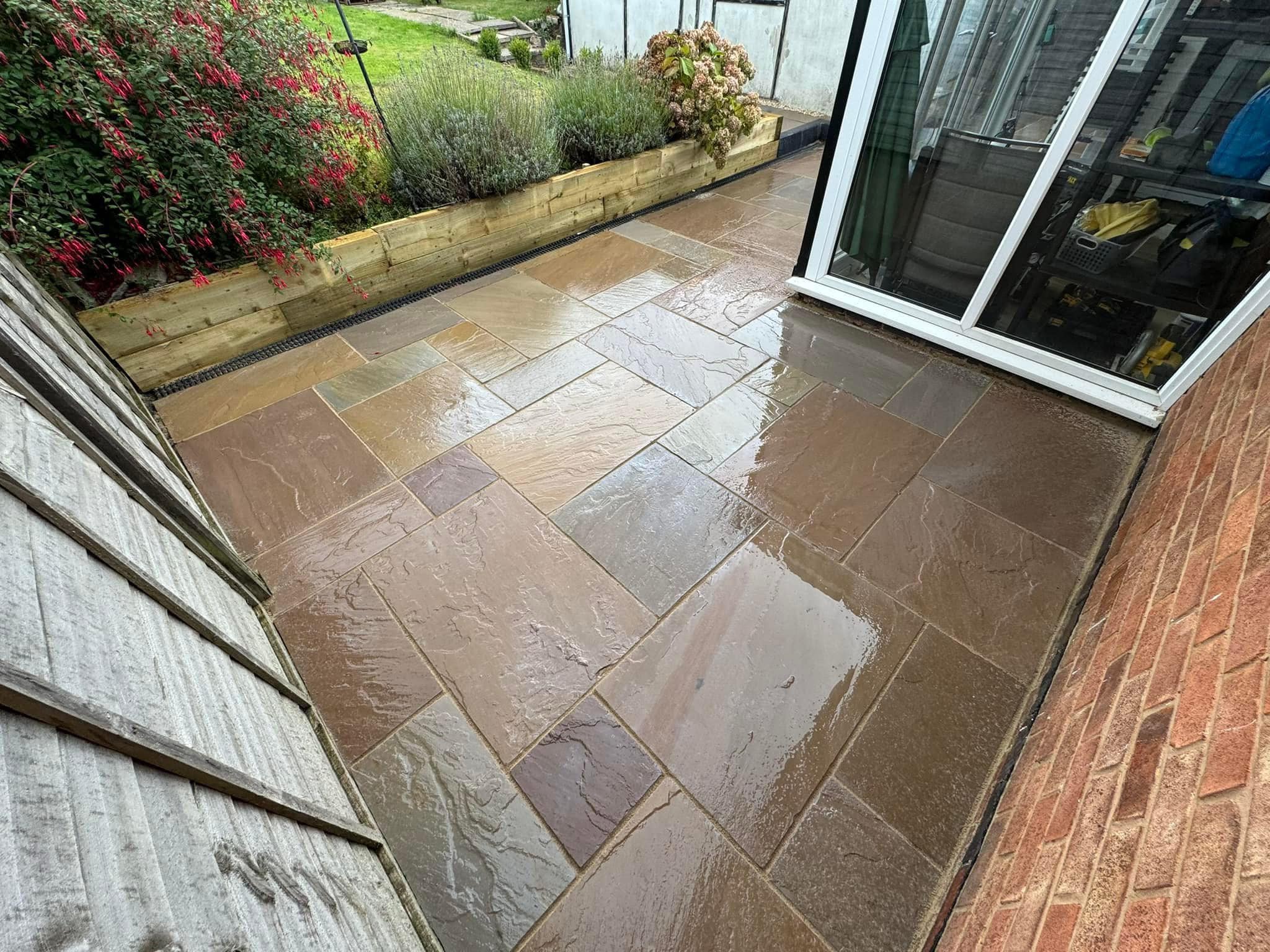 Sandstone patio running up to a conservatory, with raised sleeper beds and planting alongside